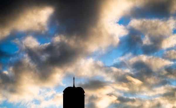  一座钟楼的剪影映衬着多云的蓝色和金色的日出.